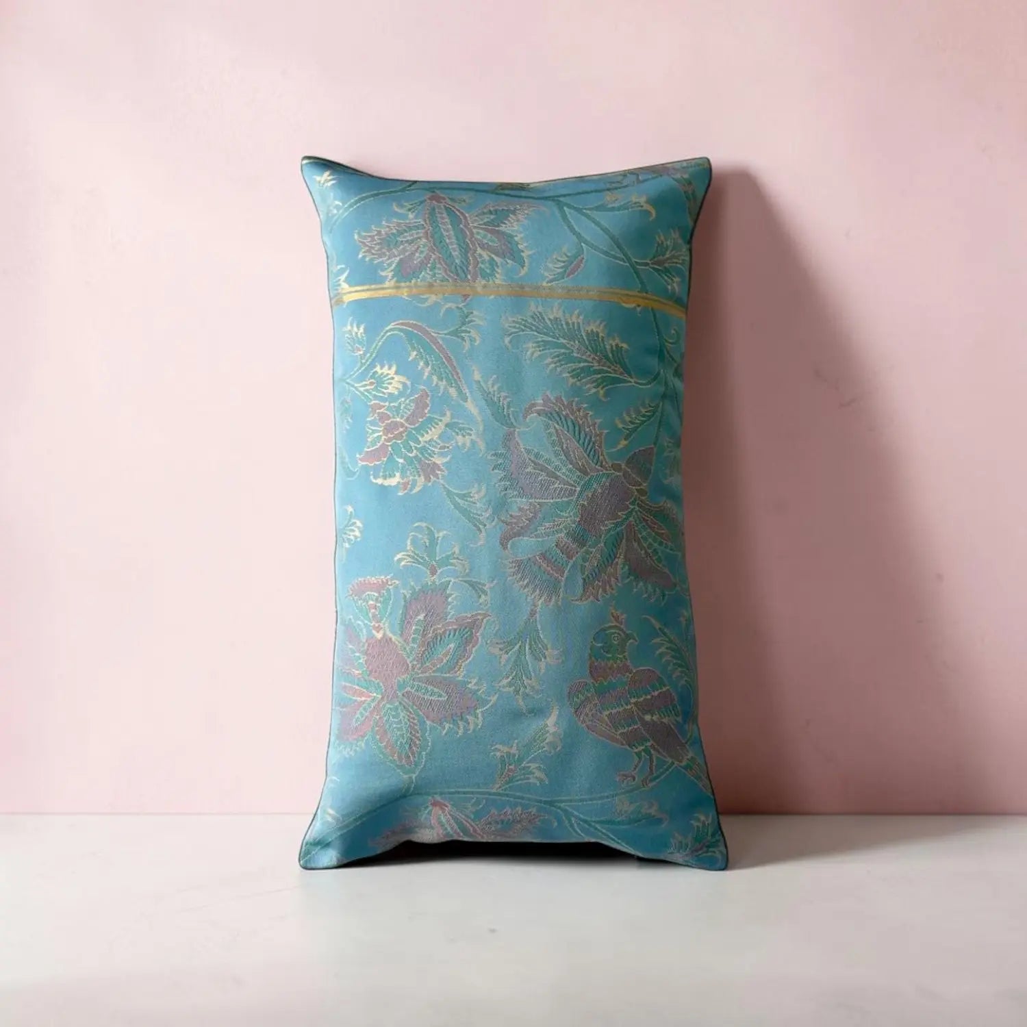 Decorative blue cushion with floral and bird patterns on a pink background