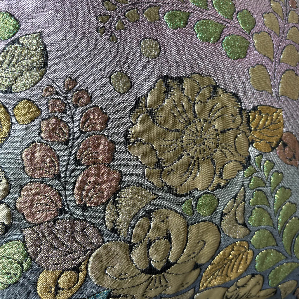 Close-up of floral embroidery with green, brown, and gold colors on a textured fabric background.