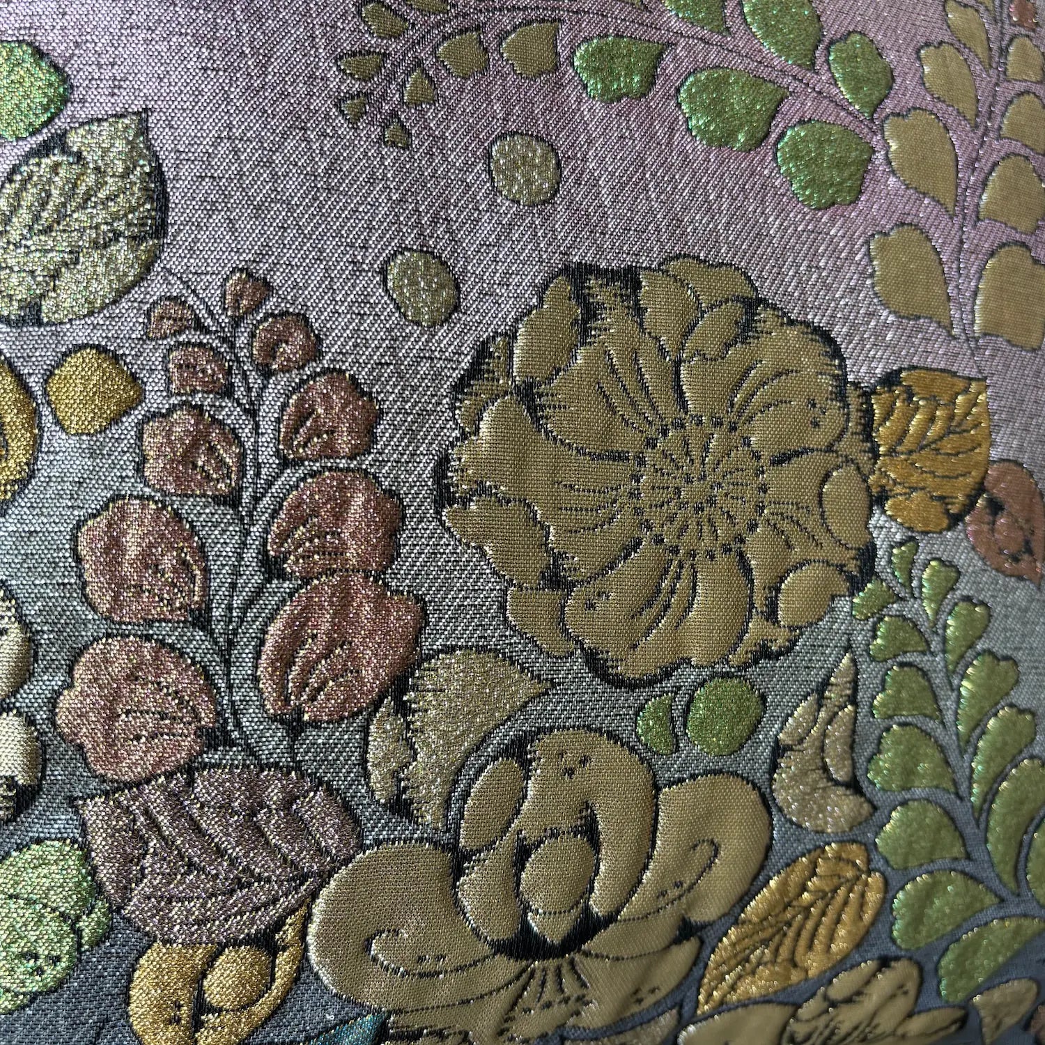 Close-up of floral embroidery with green, brown, and gold colors on a textured fabric background.