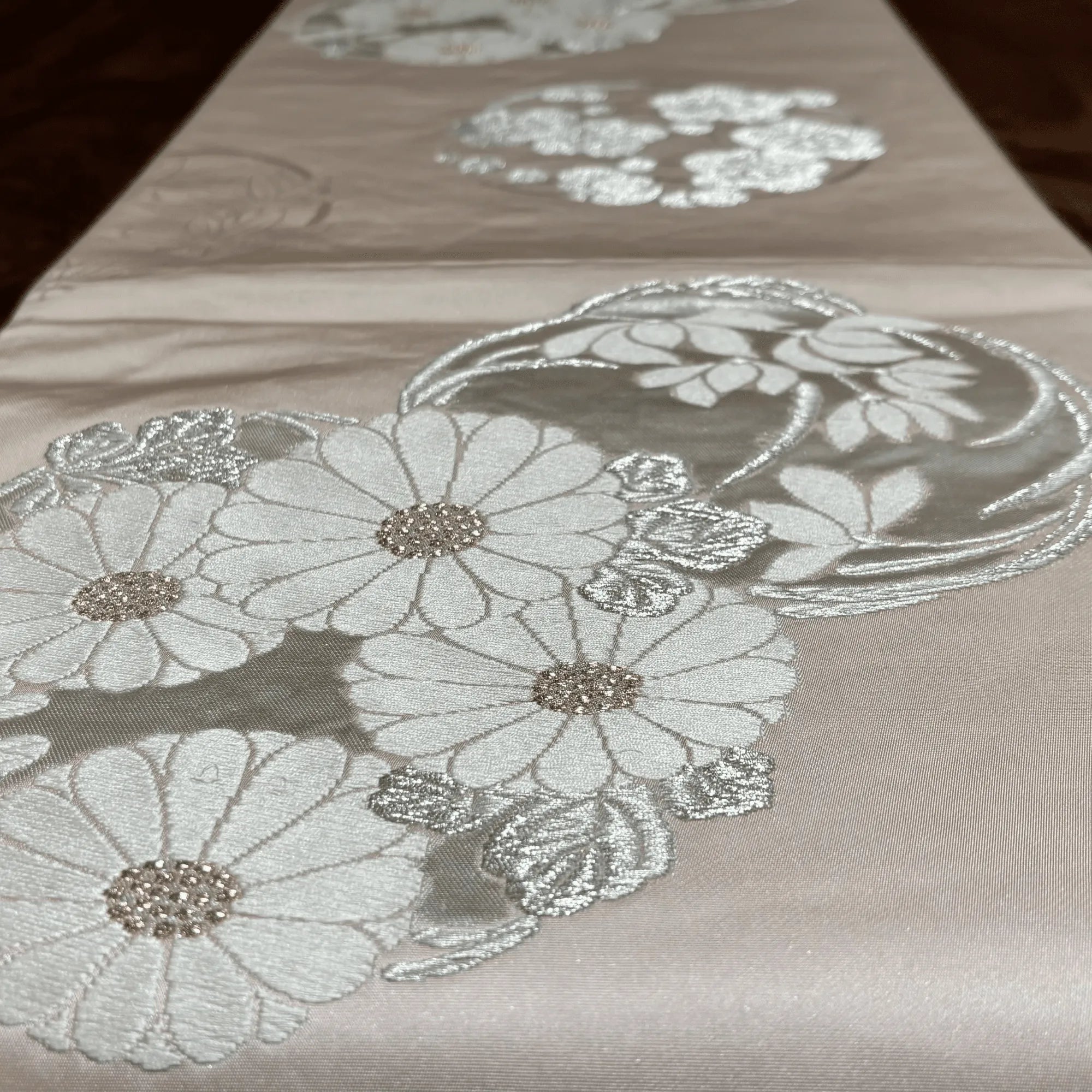 Embroidered floral table runner with silver thread on a wooden surface