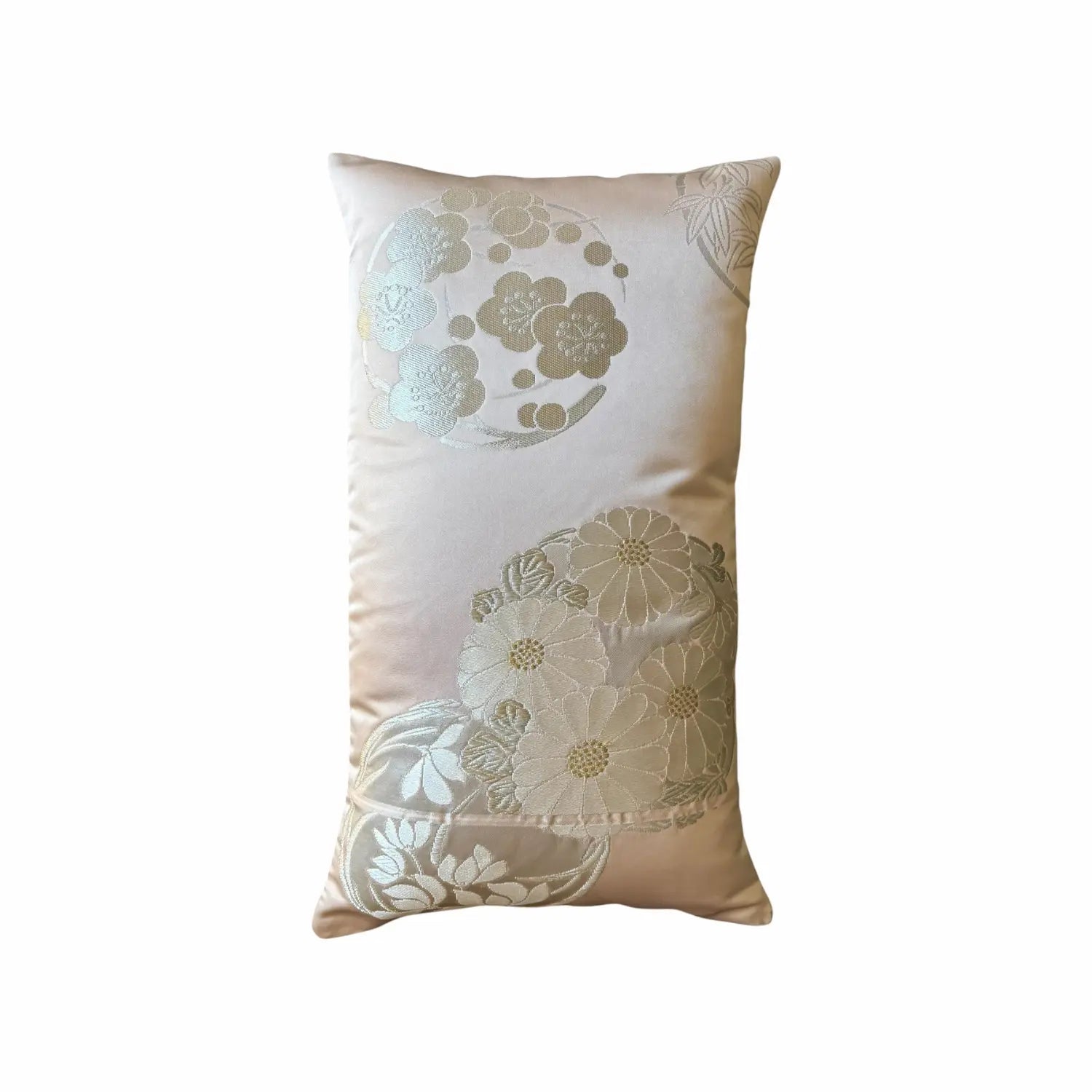 A rectangular decorative cushion in a light pink fabric with metallic gold and silver floral patterns