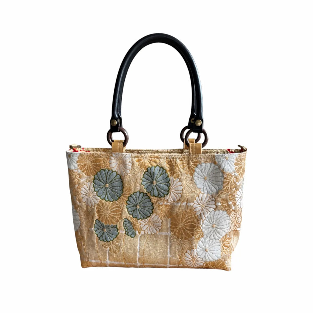 A structured handbag with a beige and white floral pattern, featuring dark blue-green chrysanthemum motifs, and dual black handles.