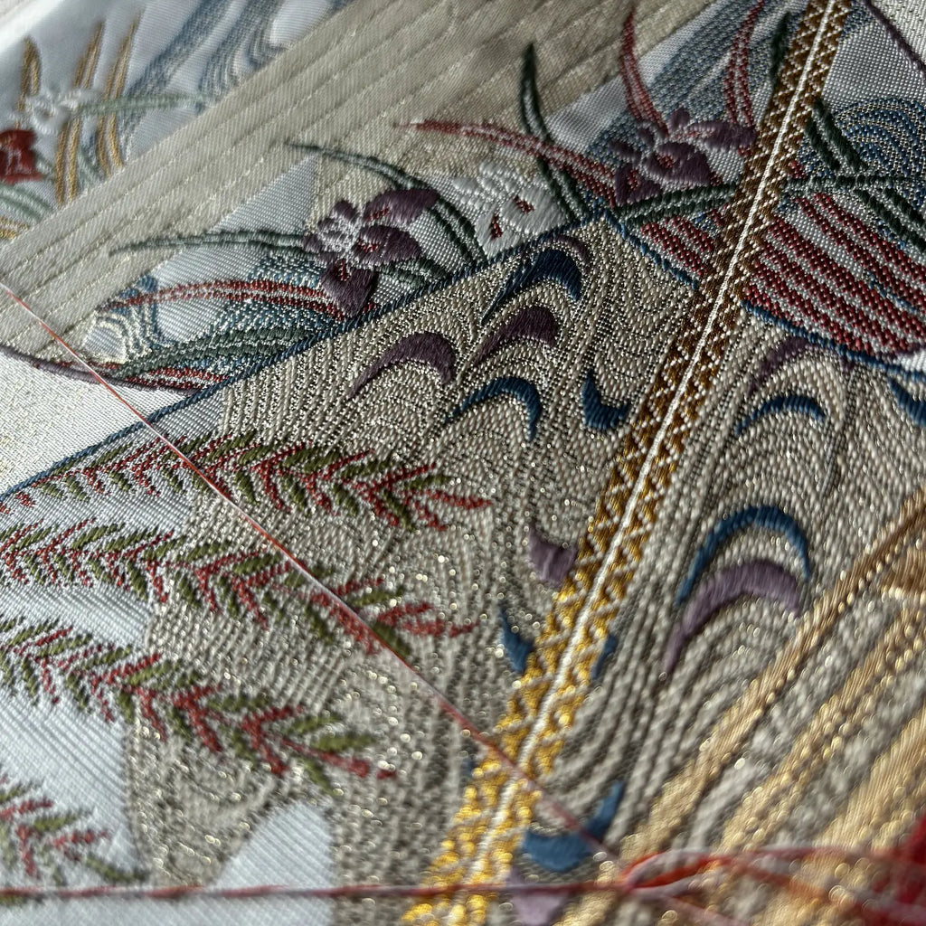 Close-up of an Kimono Obi with intricate floral and wave patterns in metallic gold, burgundy, green, blue, and purple on a light beige base.
