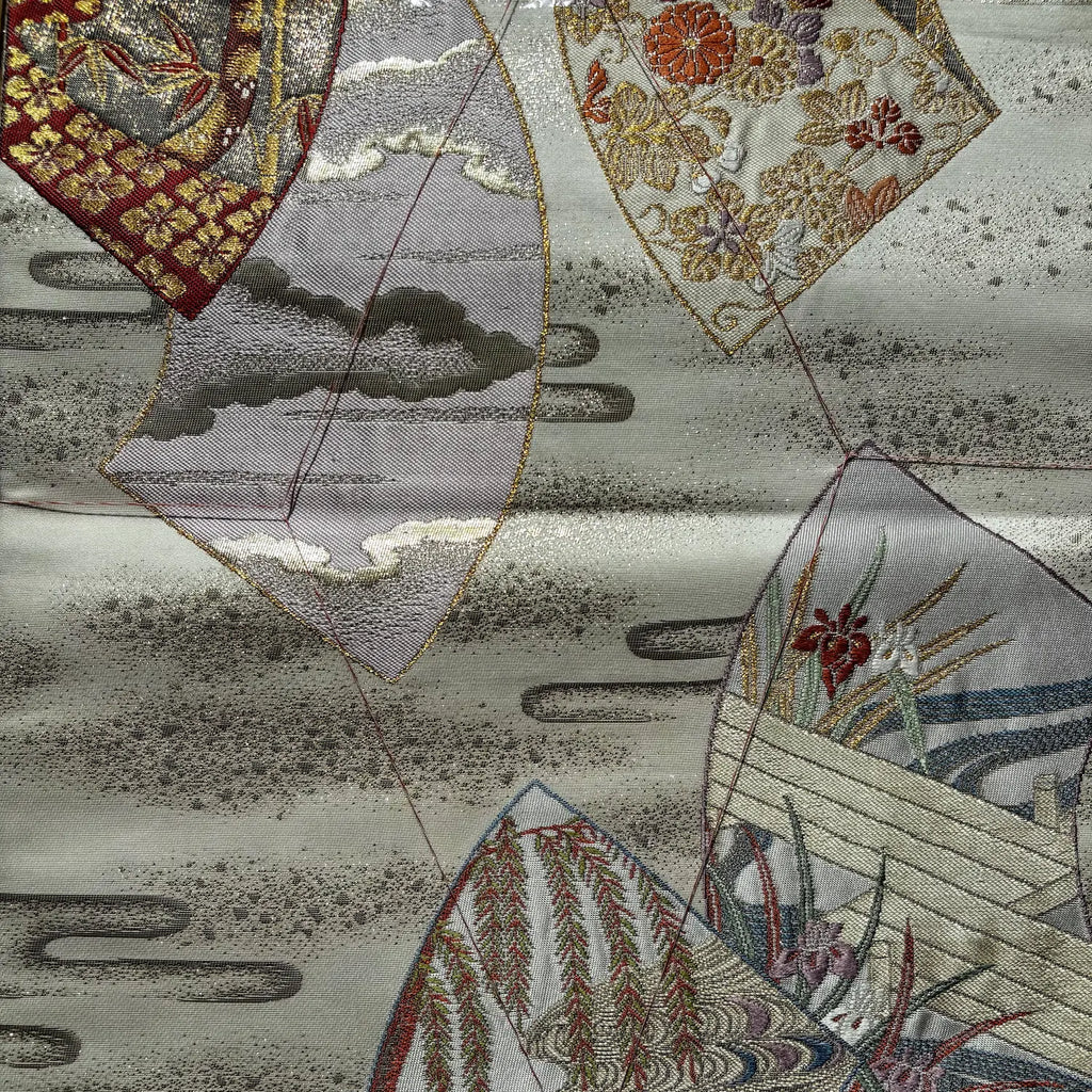 Close-up of a Japanese-style patterned Kimono Obi with embroidered patterns, featuring cloud, mountain, and floral motifs in muted gray, beige, gold, red, and blue tones.