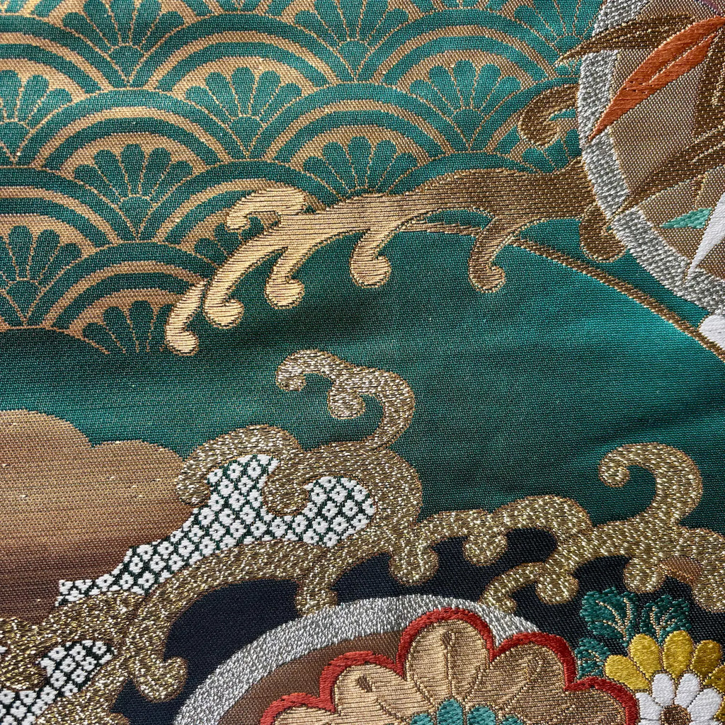 Close-up of intricately embroidered fabric with gold and brown patterns on a teal background.