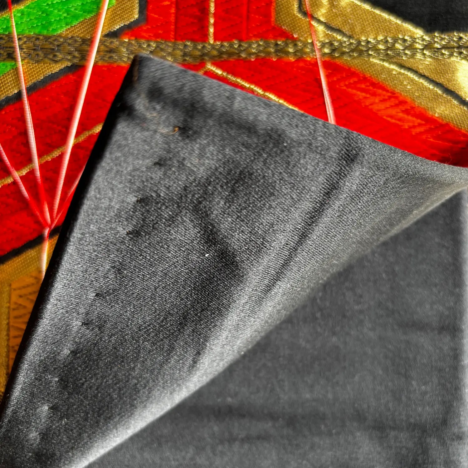 A close-up of a black textured fabric, shown folded over to reveal its matte, slightly suede-like or velvety surface. 