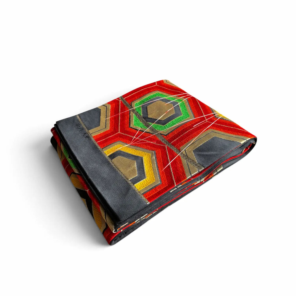 A folded Obi, featuring a vibrant geometric pattern with red, green, yellow, and black sections, displayed on a clean white background.