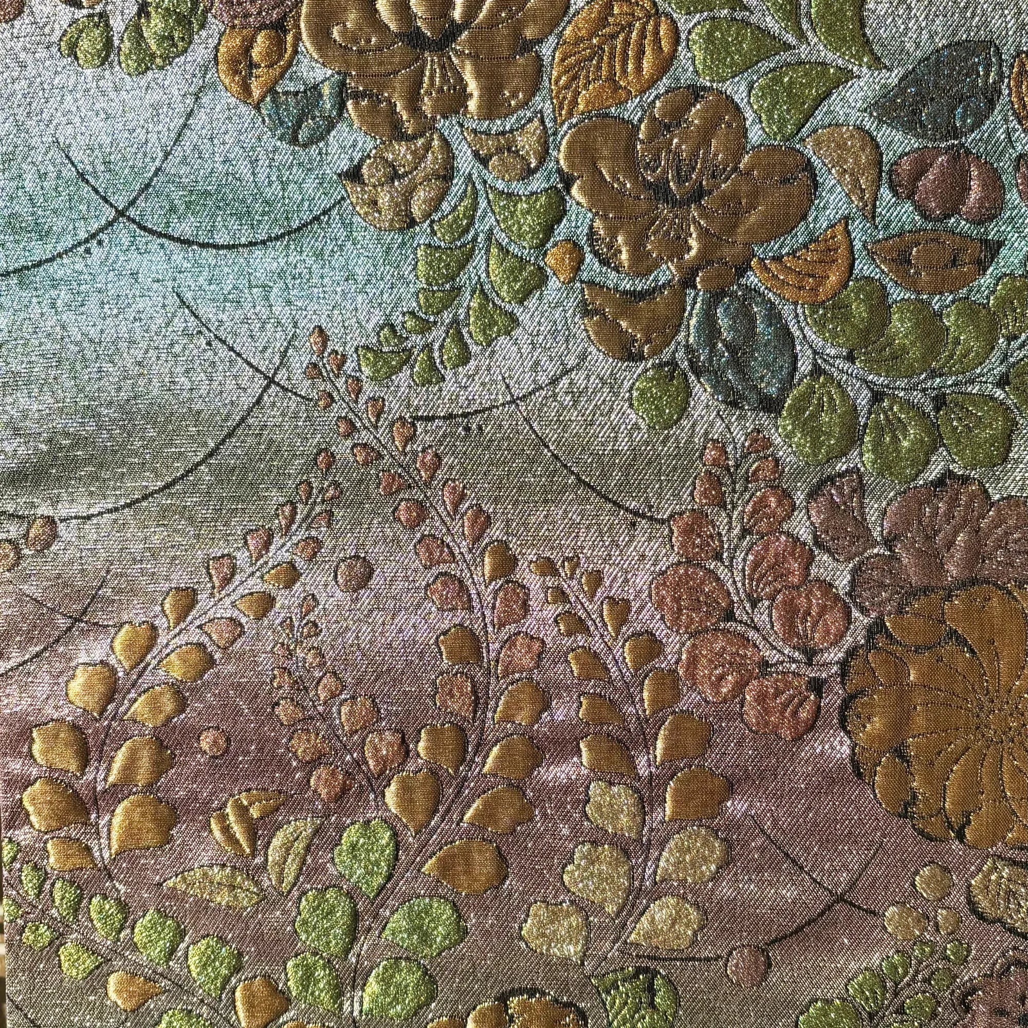 Close-up of embroidered floral pattern with gold, green, and brown colors on a fabric.