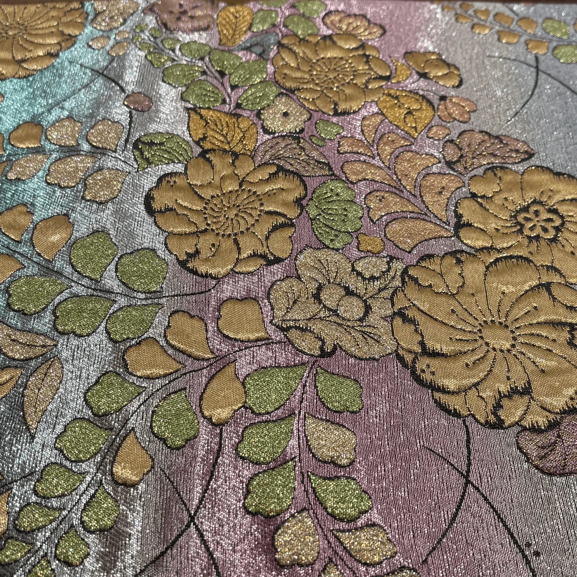 Close-up of floral embroidery with green and gold leaves on a textured fabric background.