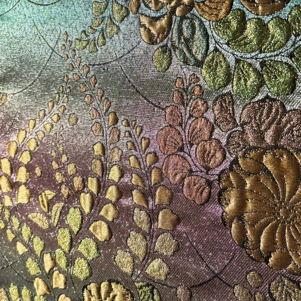 Close-up of an embroidered fabric with floral patterns in gold, green, and brown.