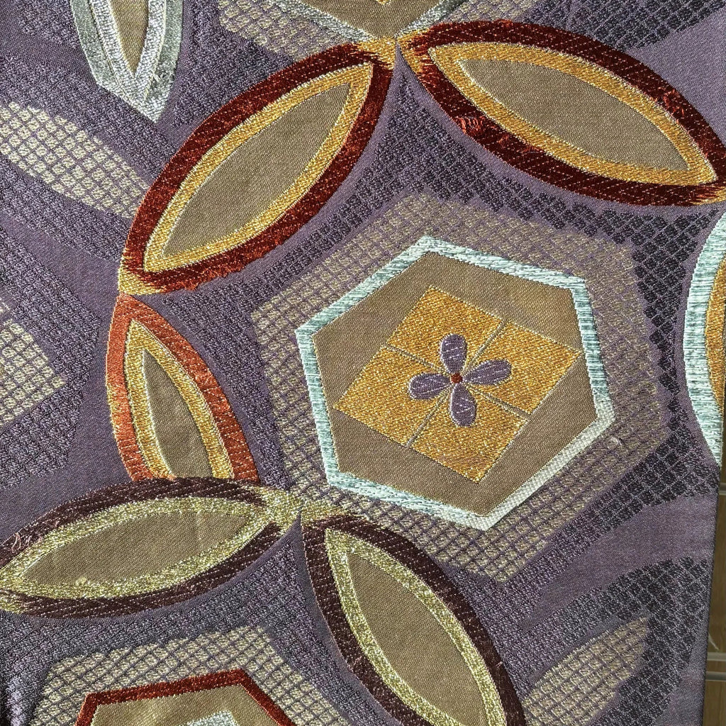 Close-up of a silk fabric with geometric patterns in purple, gold, and brown.
