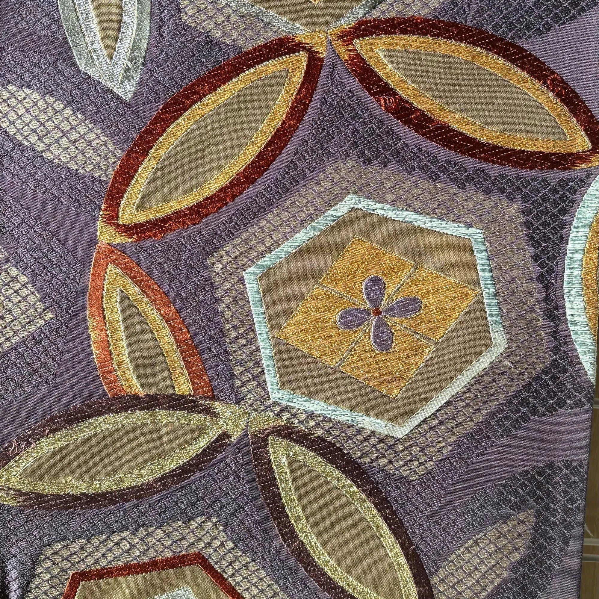 Close-up of a silk fabric with geometric patterns in purple, gold, and brown.