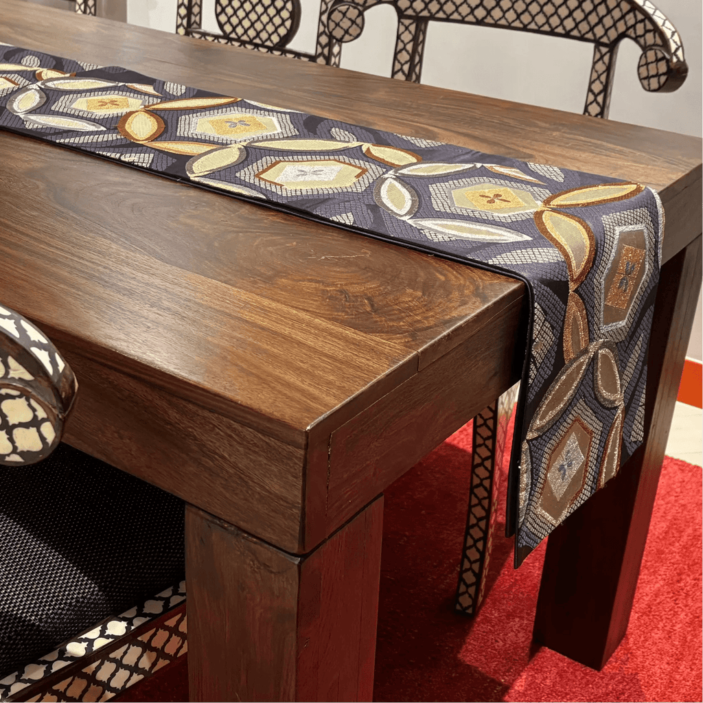 Wooden dining table with a patterned table runner on a red carpet