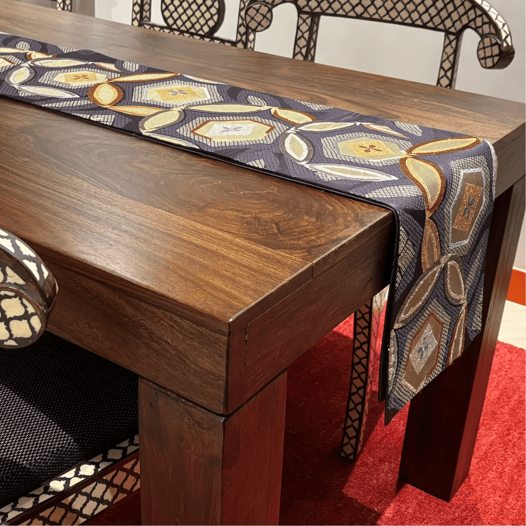 Wooden dining table with a patterned table runner on a red carpet