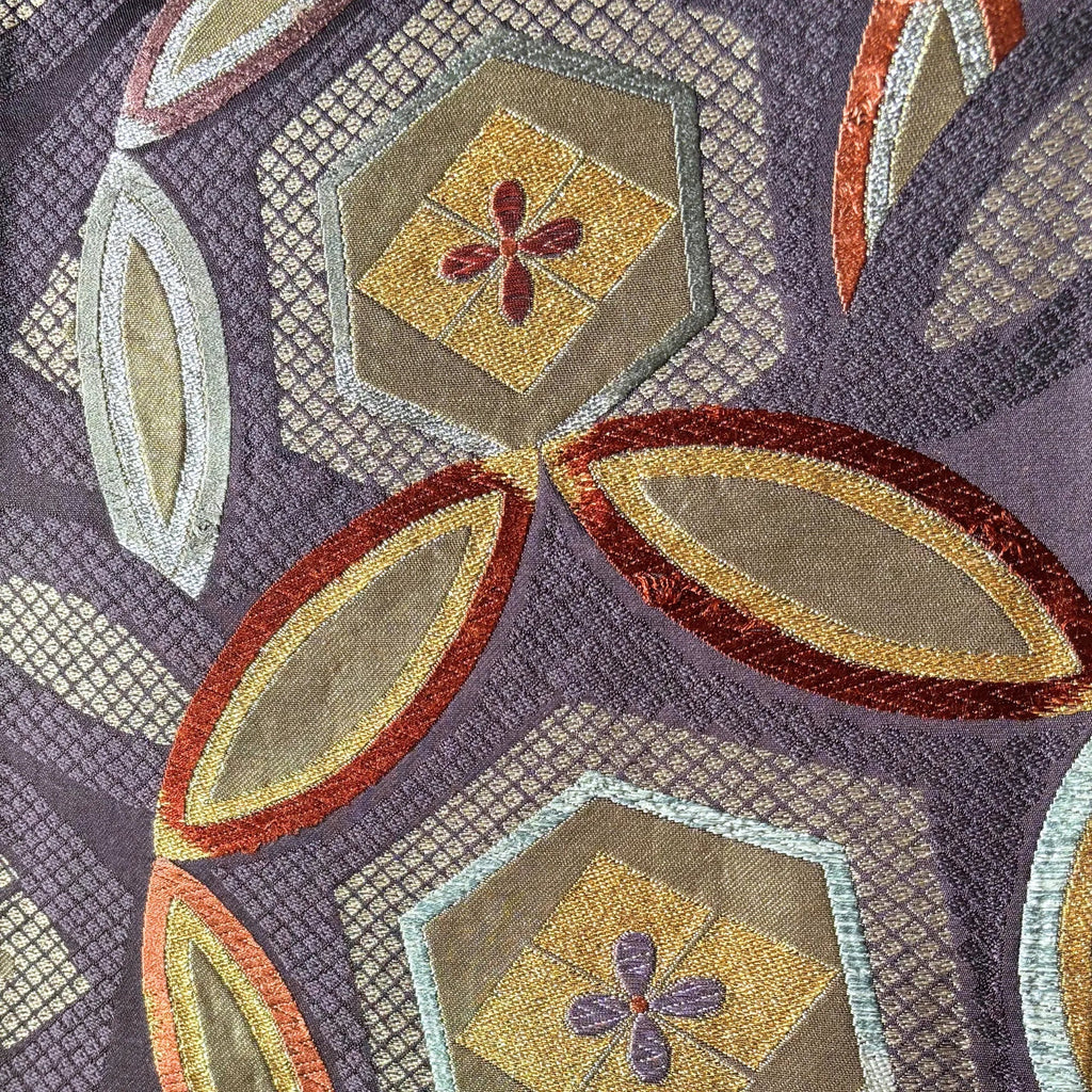 Close-up of a patterned silk with geometric shapes and floral elements on a purple background.