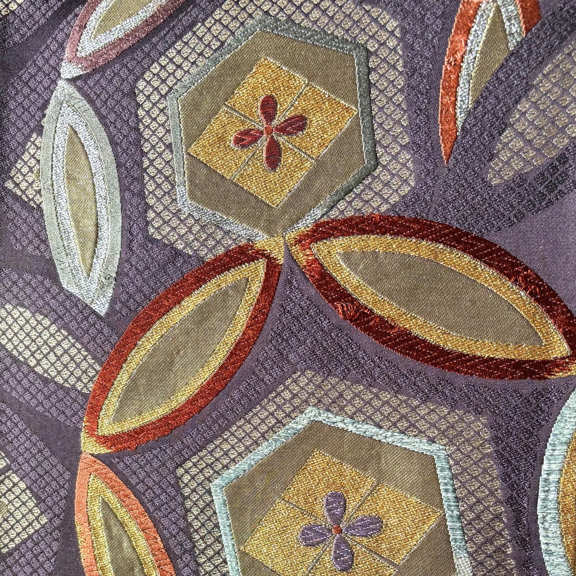 Close-up of a patterned silk with geometric shapes and floral elements on a purple background.