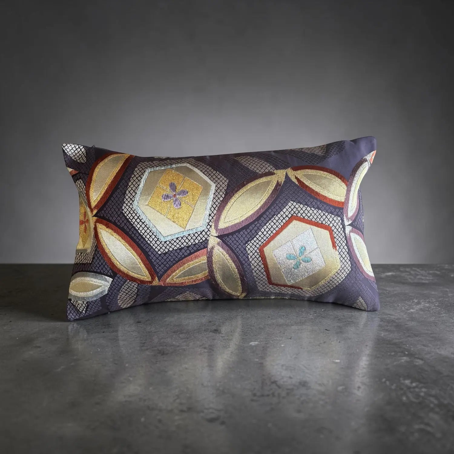A rectangular decorative cushion with an intricate geometric pattern in gold, purple, blue on a dark background.
