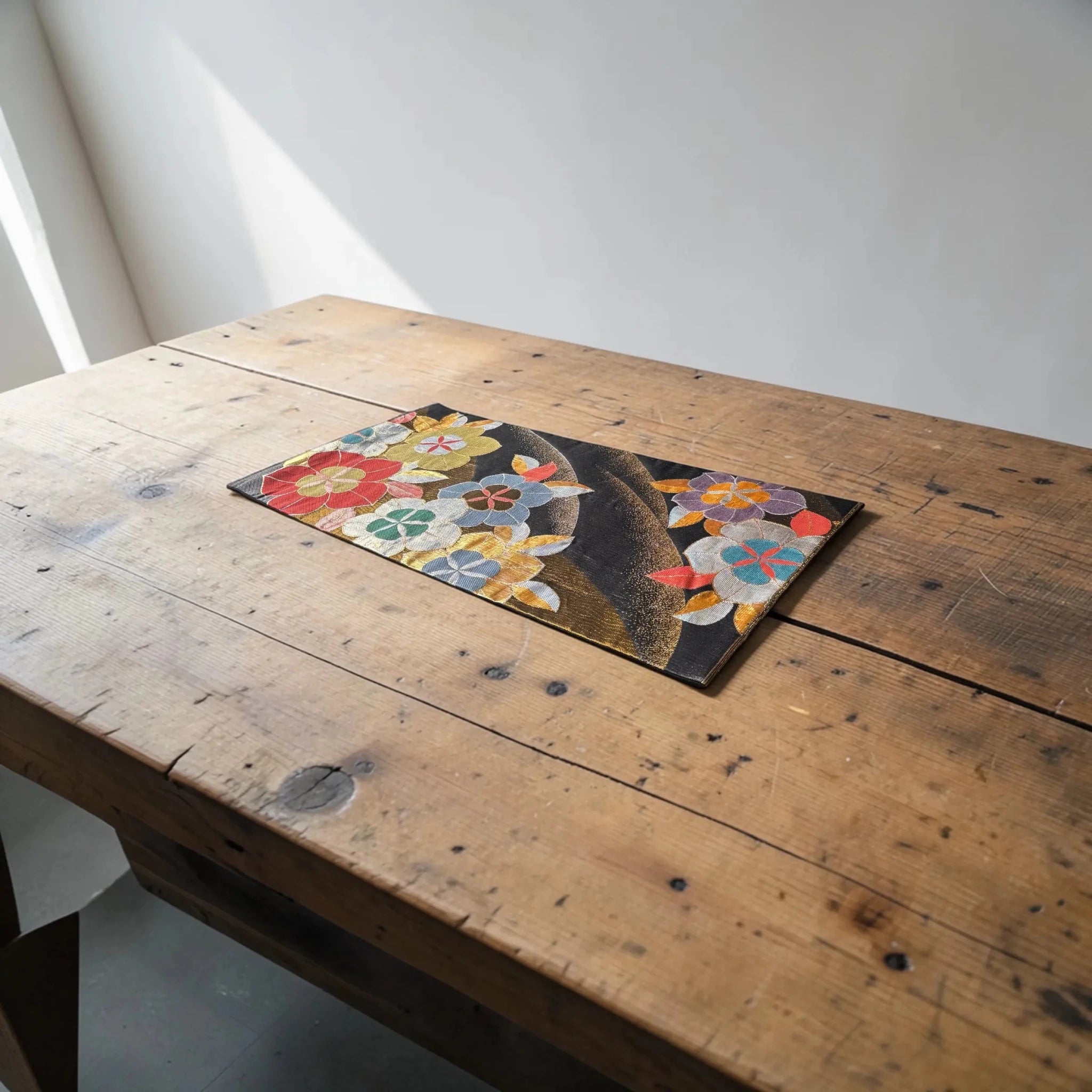 Floral silk Obi on a wooden table with a white wall background