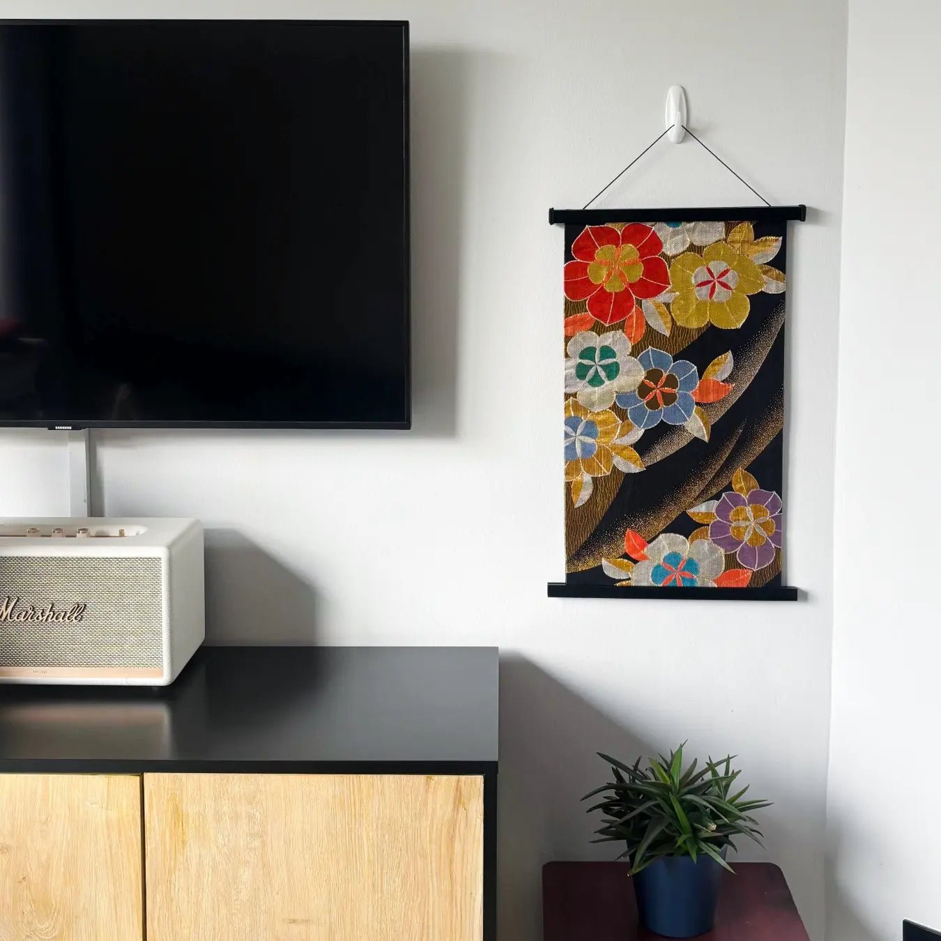 Decorative floral wall hanging above a TV in a living room setting.