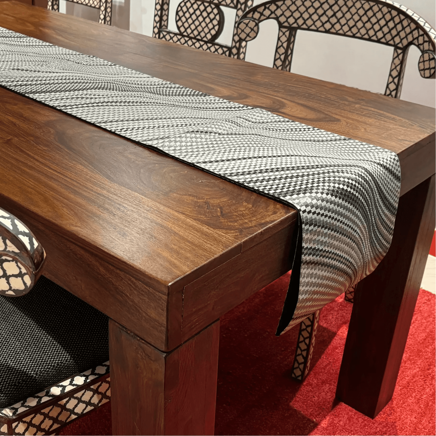 Wooden dining table with a checkered table runner on a red carpet