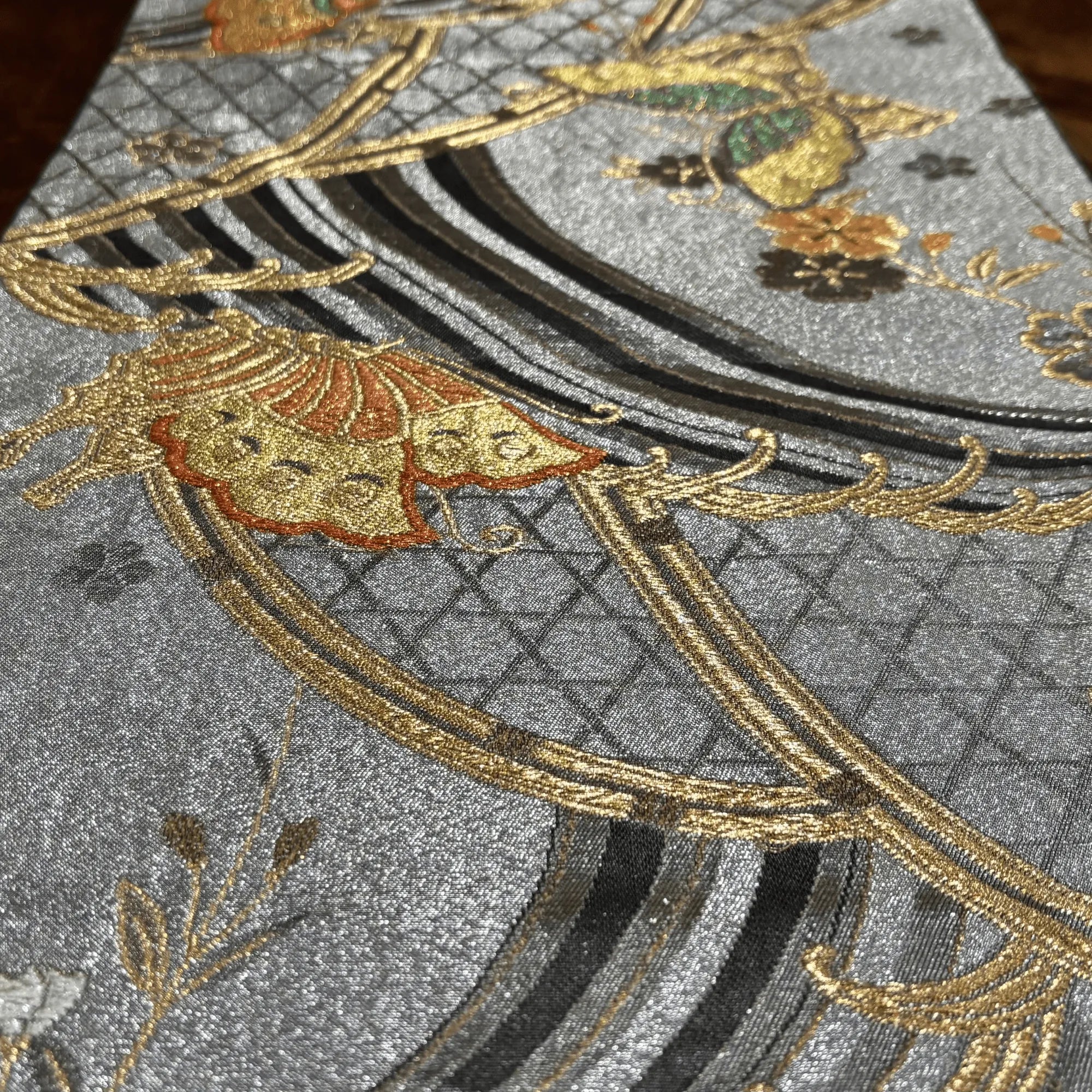 Close-up of embroidered fabric with gold and black patterns on a silver background
